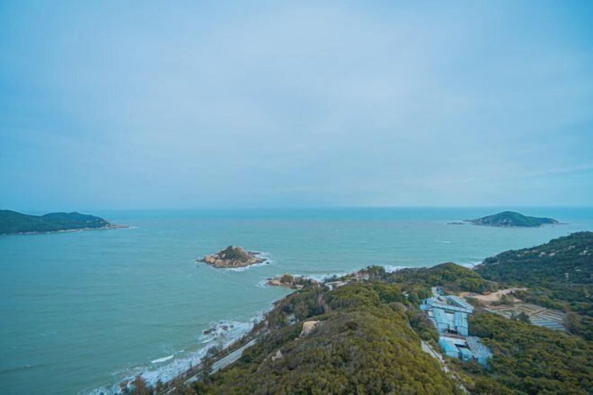 A coastal landscape with a small island, a road, and a building with blue roofing.