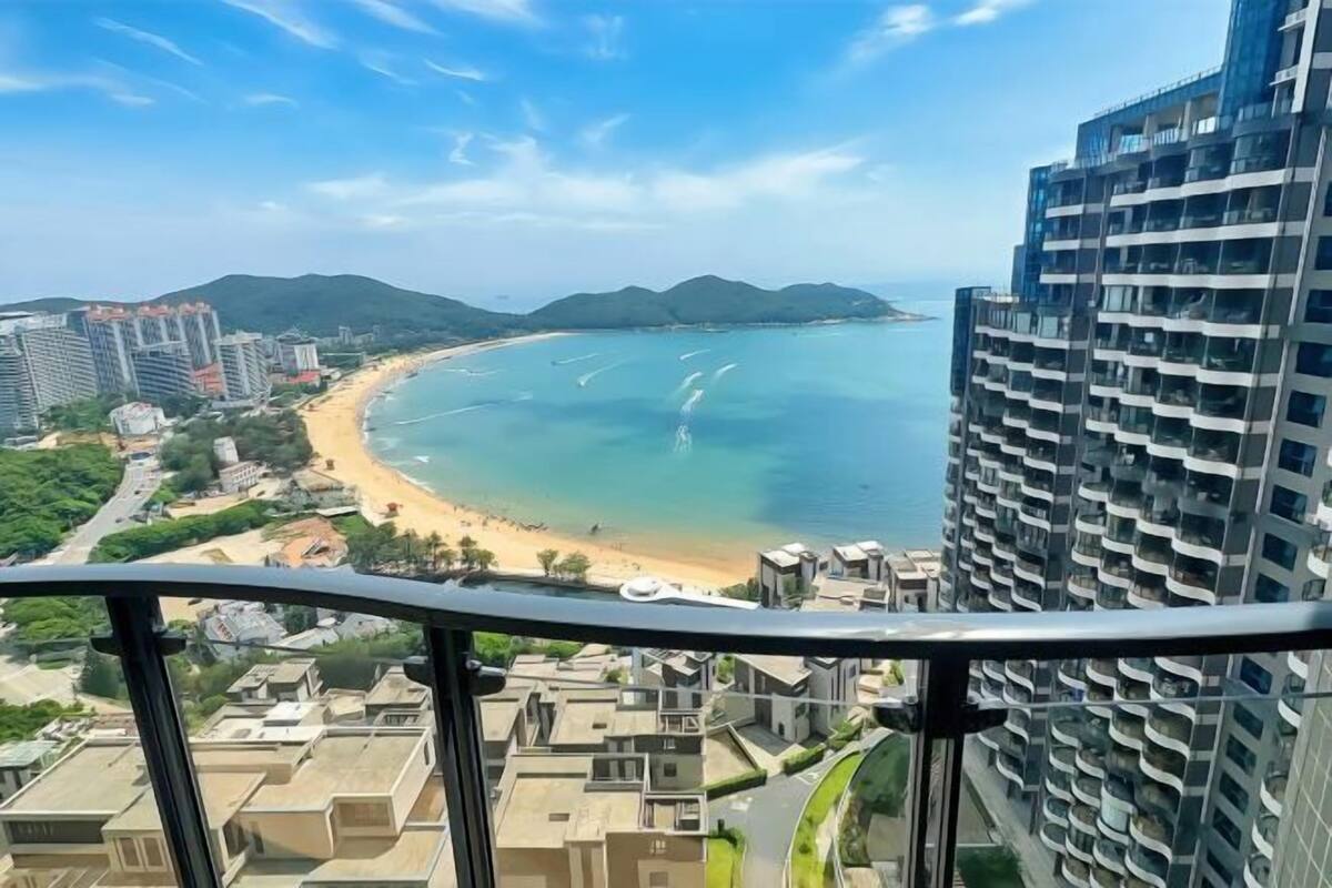 Vista costera desde un edificio alto, con una playa y montañas al fondo.