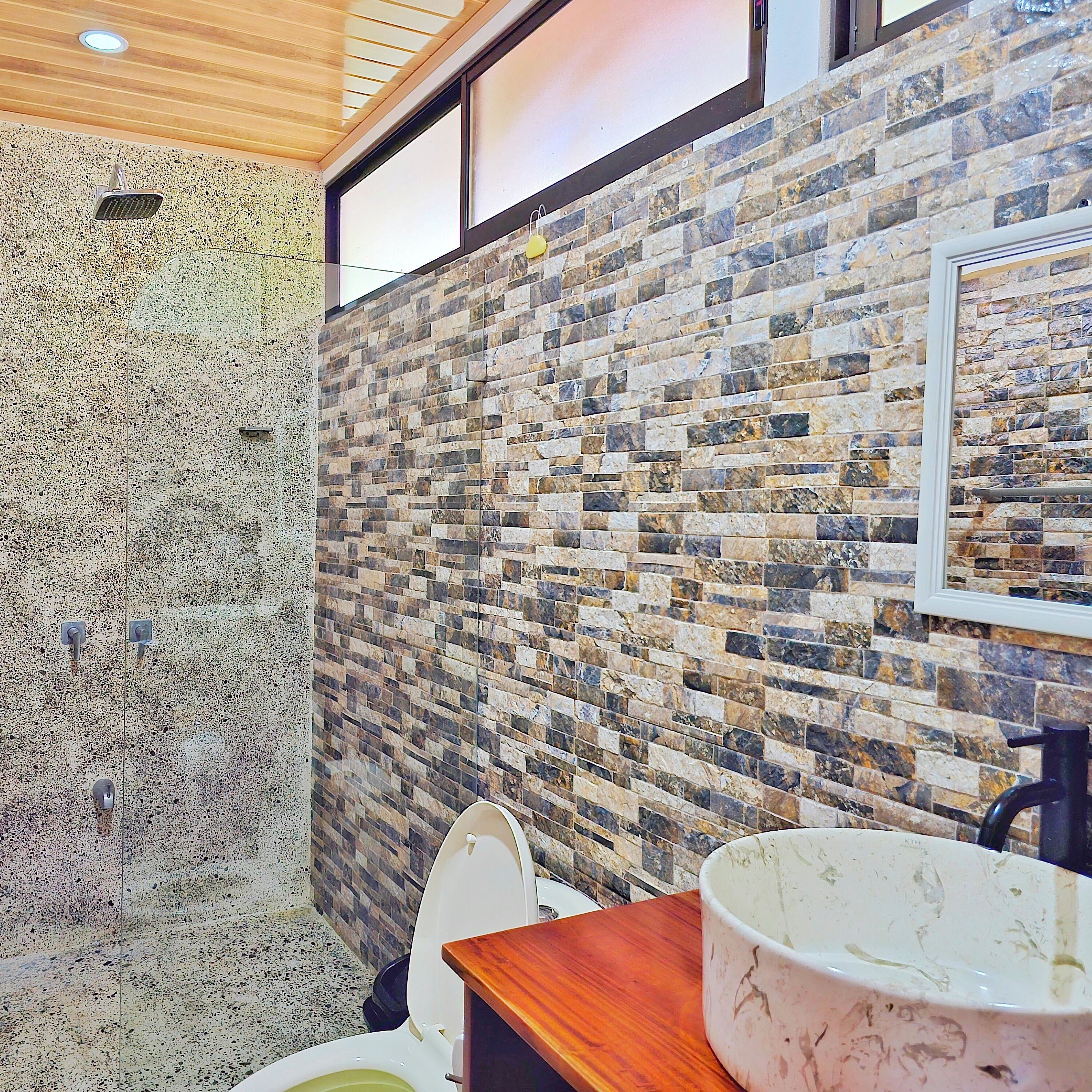 A bathroom with a stone wall, a toilet, and a sink with a basin.