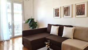 Ein Wohnzimmer mit einem braunen Sofa, einem Glastisch und einem Blumentopf. An der Wand hängen drei gerahmte Bilder.
