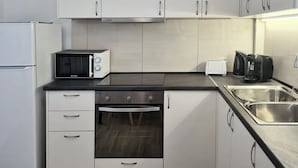 Eine kompakte Küche mit weißen Schränken, einer eingebauten Mikrowelle, einem Toaster, einer Kaffeemaschine und einer Spüle aus Edelstahl.