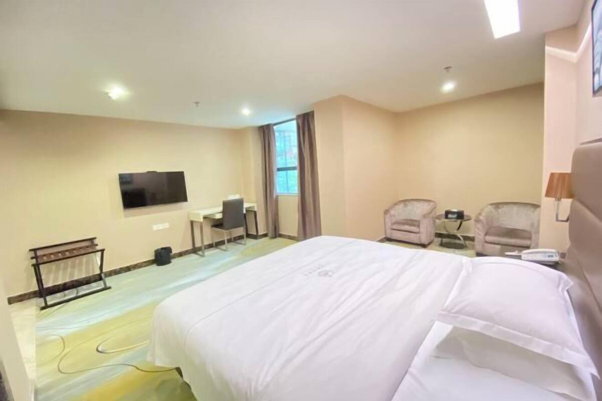 A hotel room with a bed, desk, chairs, a TV, and a window.