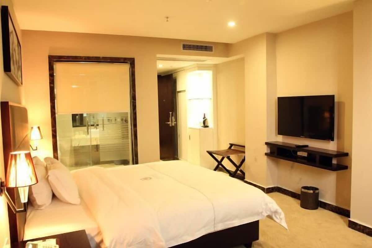 A hotel room with a bed, a television, a desk, and a bathroom visible through an open door.