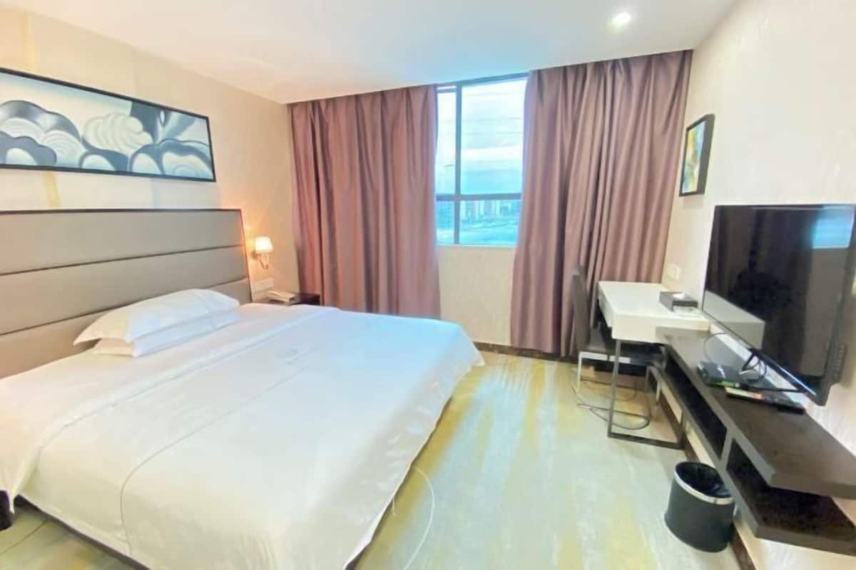 A hotel room with a bed, a desk, a television, and a window with curtains.