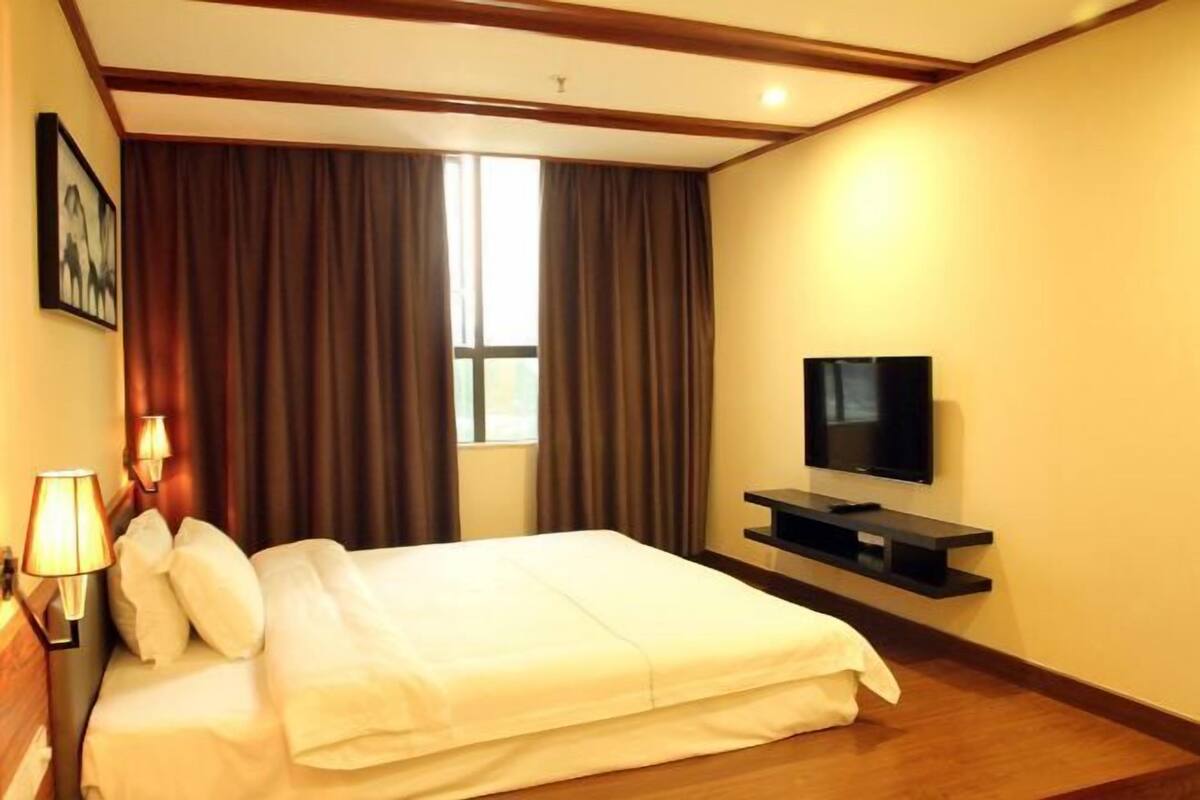 A hotel room with a bed, a television, a window with curtains, and a wall-mounted shelf.