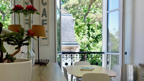A modern kitchen with a wooden countertop, white cabinets, and a view of the outdoors through large windows. - Latin Quarter - Jardin des plantes (Paris)