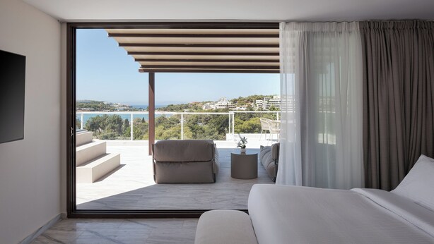 Ein modernes Schlafzimmer mit einer großen Schiebetür, die auf einen Balkon mit Blick auf das Meer und die Gebäude führt.