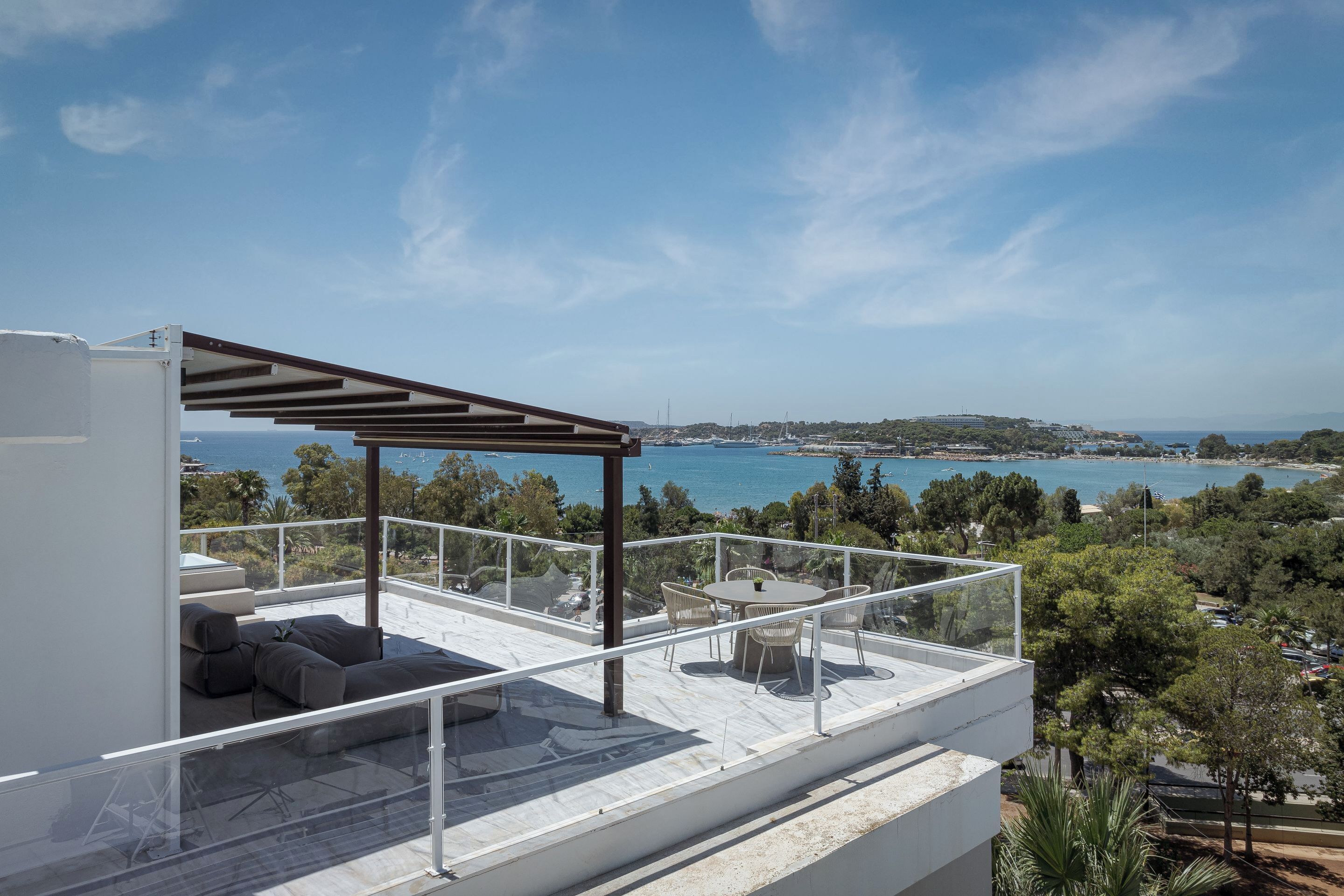 A modern outdoor terrace with a pergola, seating, and a table, overlooking a coastal landscape.