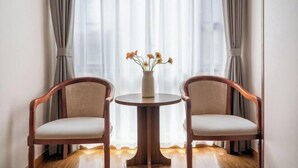 A room with two wooden chairs and a small round table, a vase with flowers, and sheer curtains. - Kunming Xiangyi Business Hotel (Kunming)