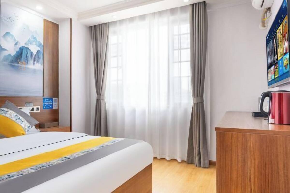A hotel room with a bed, a desk, a painting, and a window with curtains.