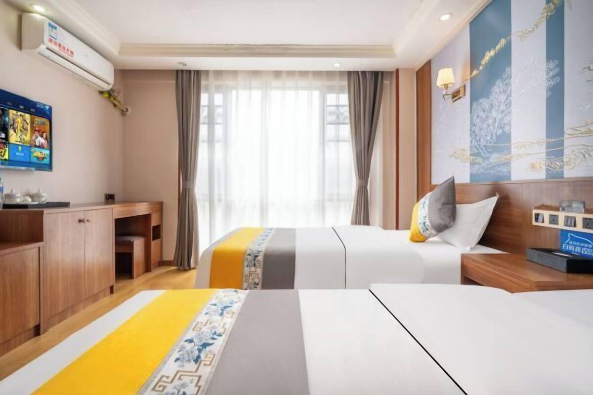 A hotel room with two beds, a desk, a TV, and a window with curtains.