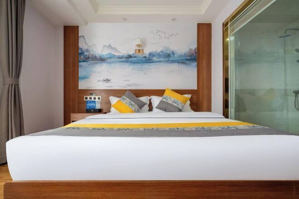 A hotel room with a bed, a painting on the wall, and a window.