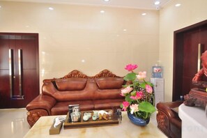 A lobby with a brown leather sofa, a marble table with a tray of items, and a vase of flowers. - Kunming Xiangyi Business Hotel (Kunming)