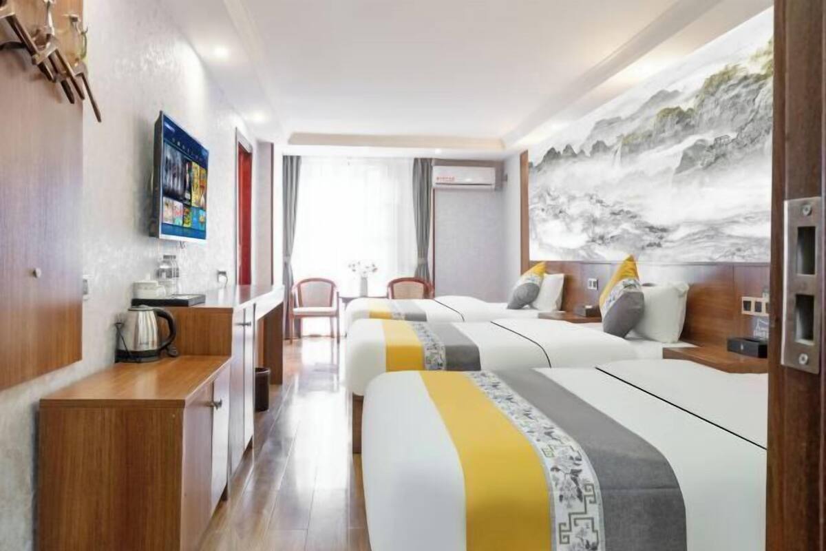 A hotel room with two beds, a wooden desk, a TV, and a painting of a mountainous landscape.