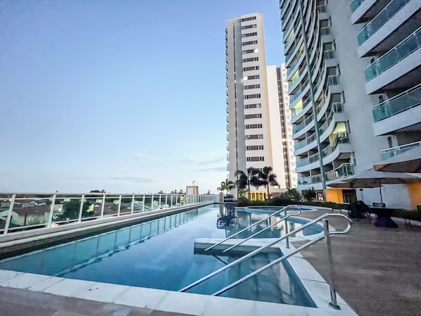 A swimming pool with a glass barrier, surrounded by modern high-rise buildings.