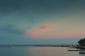 Un paysage côtier avec une mer calme, un petit bateau et une jetée bordée de bâtiments.