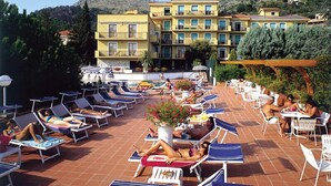 A rooftop pool area with sun loungers and umbrellas, surrounded by buildings with balconies and a mountainous backdrop. - I Morelli 5 Pax - One Bedroom Apartment, Sleeps 5 (Pietra Ligure)