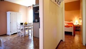 A room with a bed, a bedside table, and a nightstand. There is a window with curtains, and the room has a wooden floor.
