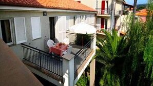A two-story building with a balcony, white shutters, and a red-tiled roof.