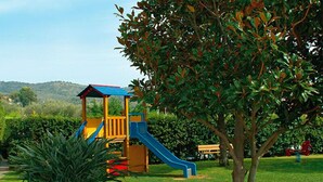 A playground with a slide and climbing area, surrounded by grass and a tree.