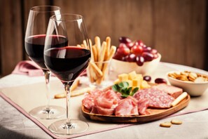 Two wine glasses filled with red wine, a wooden board with various meats, cheese, and fruits, and a bowl of crackers. - Residence Pian Dei Boschi Two-room Apartment 4 Pax (Pietra Ligure)