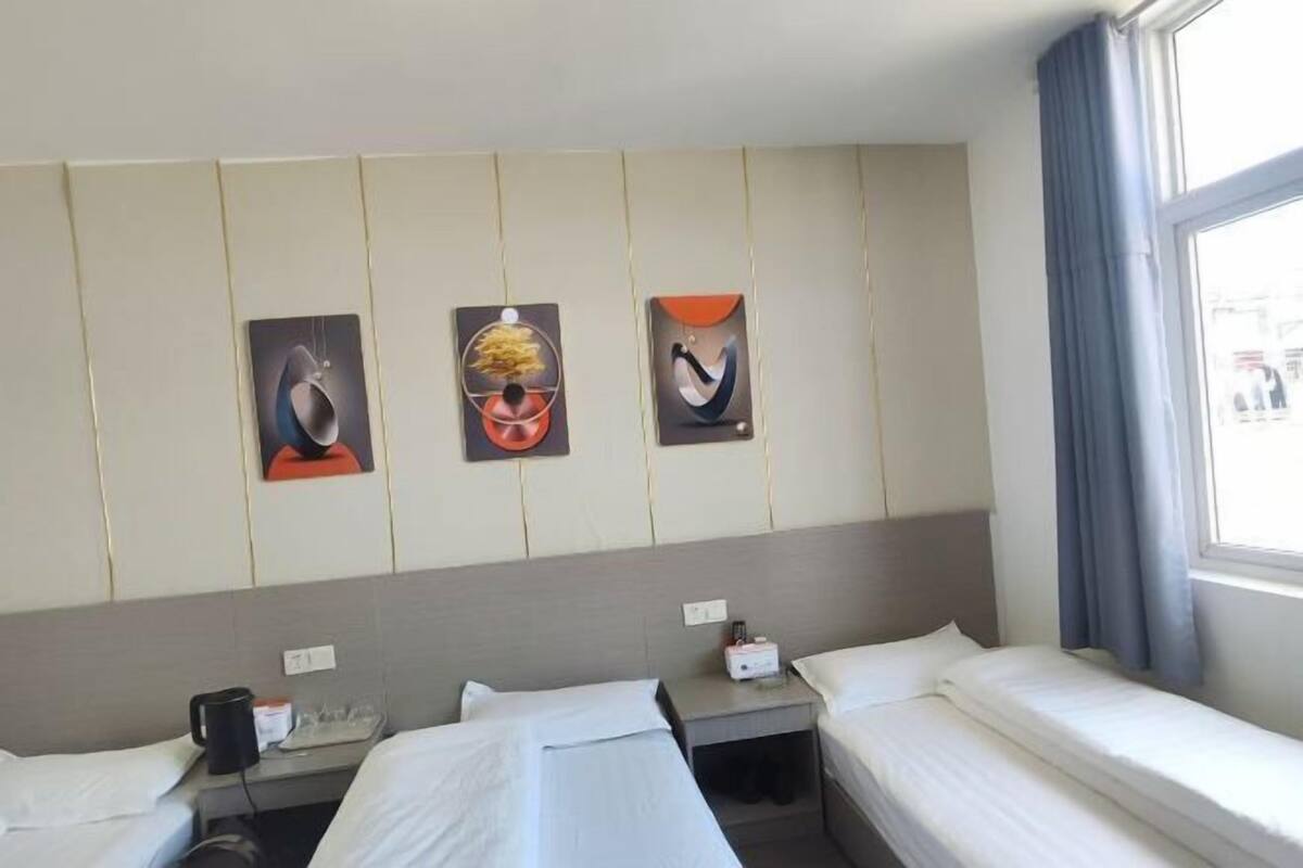 Habitación de hotel con dos camas, una ventana con cortinas y tres obras de arte colgadas en la pared.