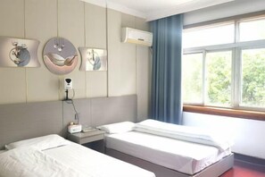 A hotel room with two beds, a bedside table, a wall-mounted air conditioner, and a window with a view of greenery. - Xiuning Limin Hotel (Xiuning)