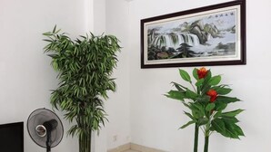 Una stanza con una grande pianta in vaso, un quadro incorniciato e una ventola.