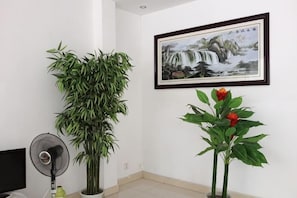 Una habitació amb una planta gran en test, un quadre amb marc i un ventilador.