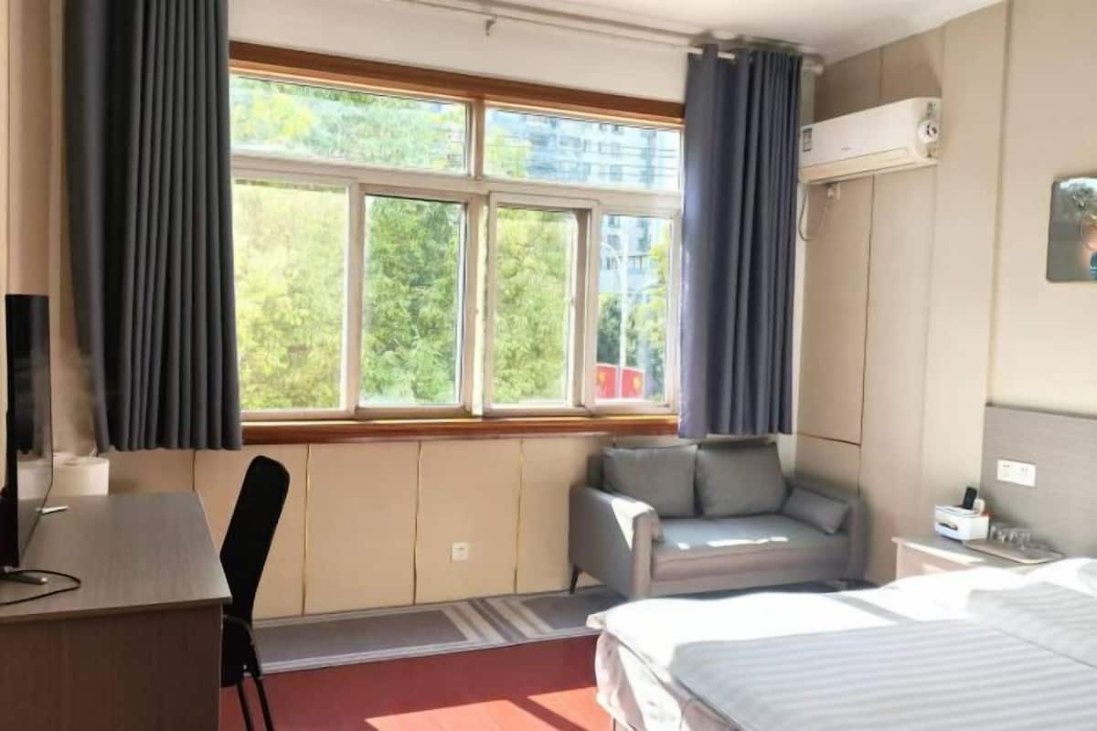 Una habitación de hotel con cama, escritorio, silla, sofá y ventana con cortinas.
