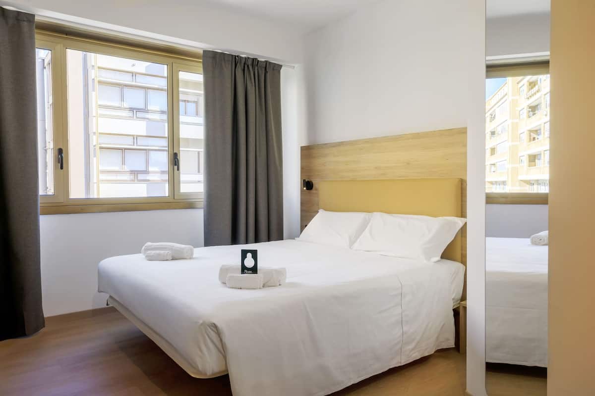 A hotel room with a bed, a window with curtains, and a view of buildings outside.