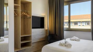 Una camera d'albergo con un letto, un armadio in legno con grucce, una TV a schermo piatto, una sedia e una finestra con tende.