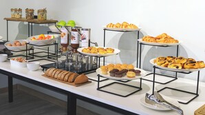 Un bufé con diversas opciones de comida, incluyendo frutas, pasteles y pan.