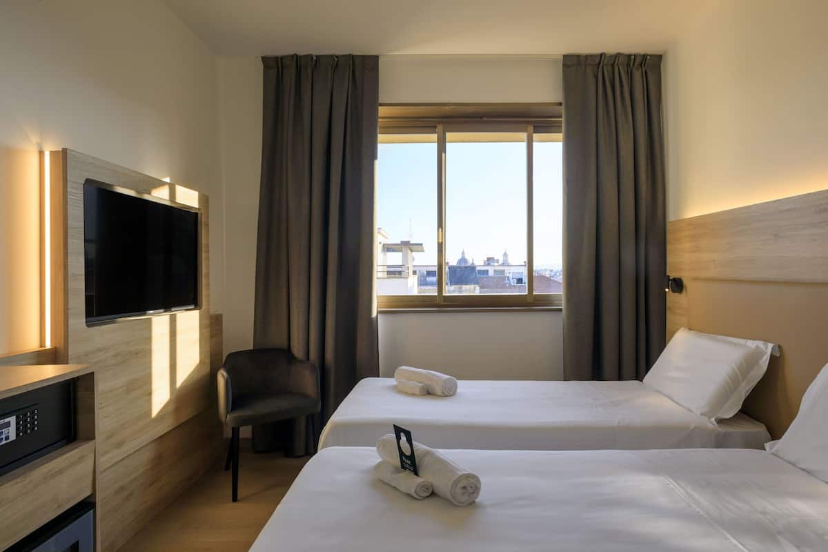 A hotel room with two beds, a TV, a chair, and a window with curtains.