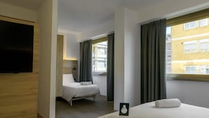 Una habitación de hotel con cama, televisión y ventana con cortinas.