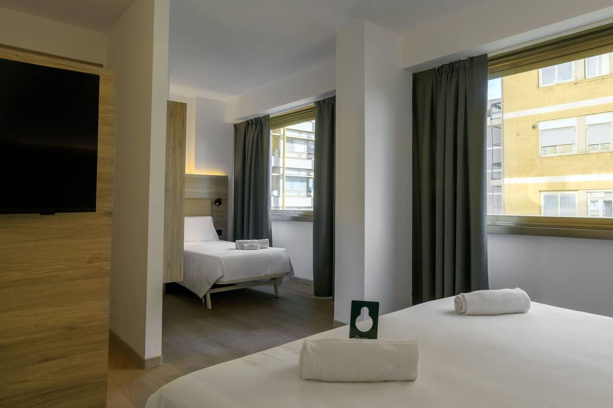 A hotel room with a bed, a TV, and a window with curtains.
