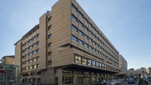 Un hotel grande y de varios pisos con un diseño arquitectónico moderno, que presenta una entrada destacada y un área techada para vehículos.