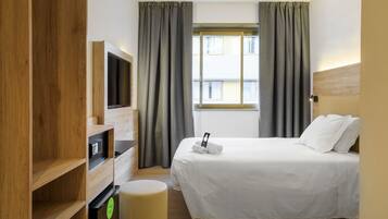 A hotel room with a bed, a TV, a wooden wardrobe, a desk, and a window with curtains.