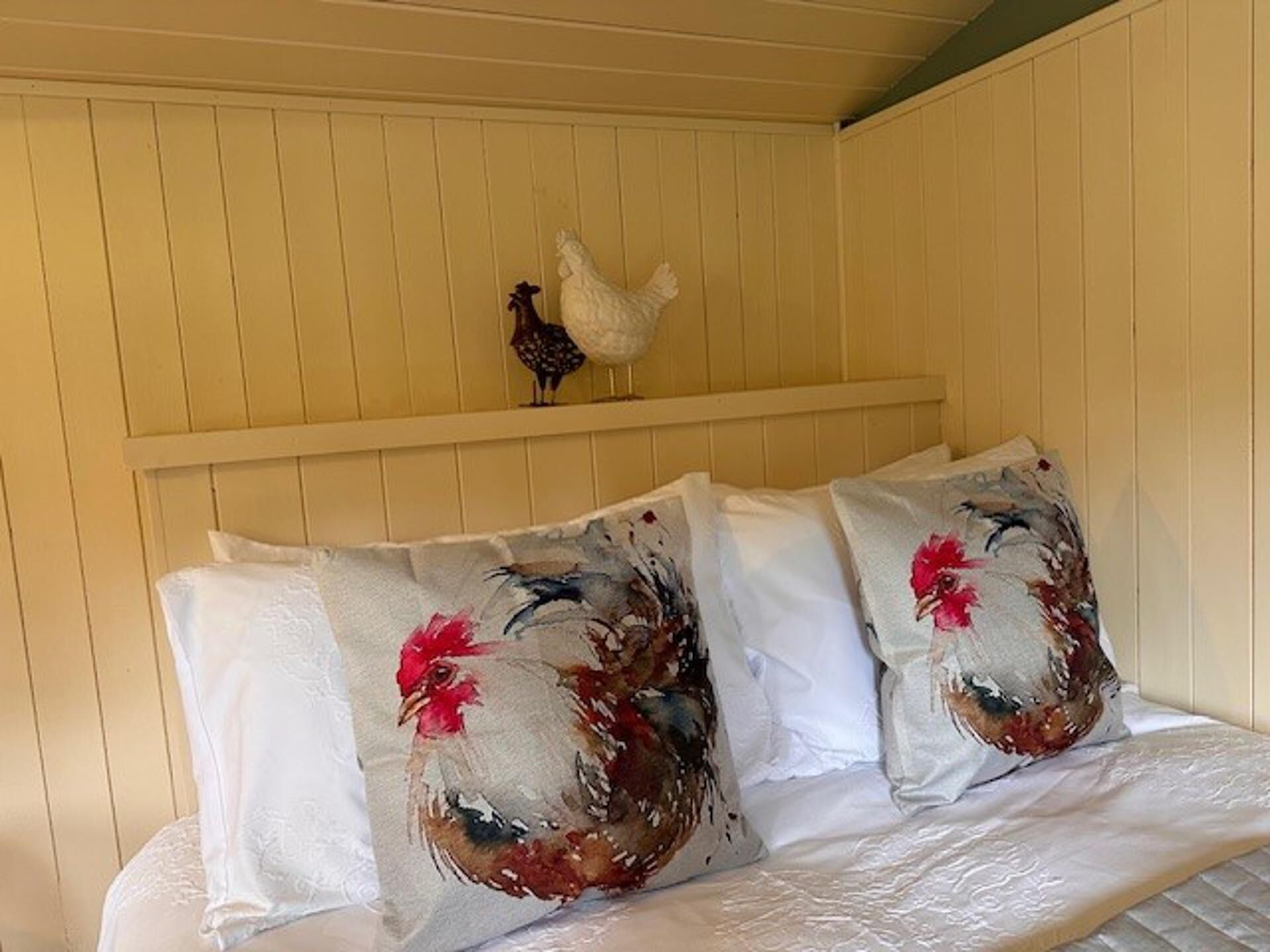 Een bed met witte lakens en twee kussens met een haan dessin.