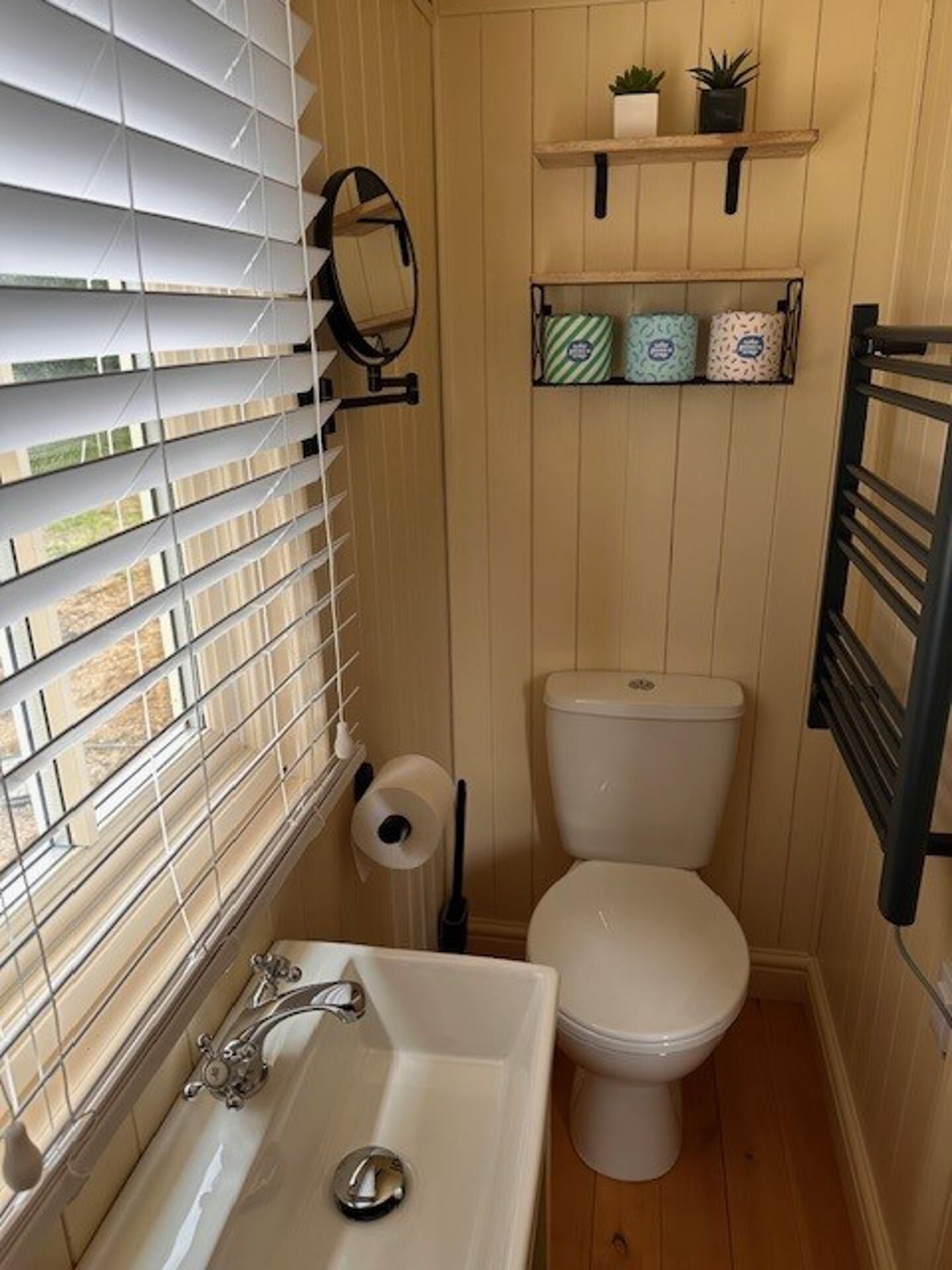 A compact bathroom with a toilet, sink, and window blinds.