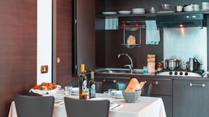 A modern kitchen with dark cabinetry, a stainless steel stove, and a dining area with a white tablecloth and chairs. - Residence Loano 2 Village  Studio Apartment 3 Pax (Loano)