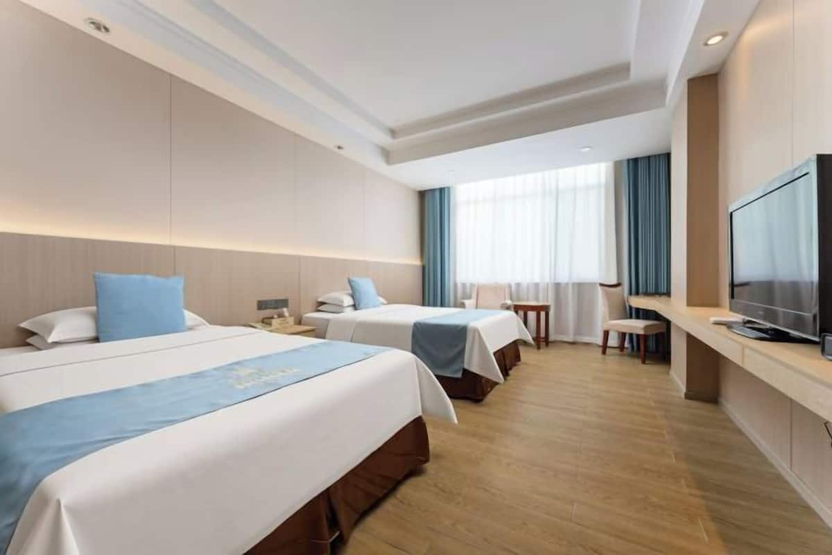 A hotel room with two beds, a TV, a desk, and a window with curtains.