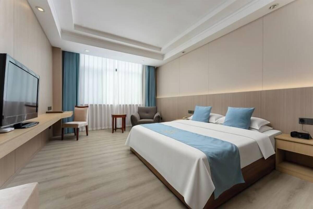 A hotel room with a bed, a desk with a television, a chair, and a window with curtains.