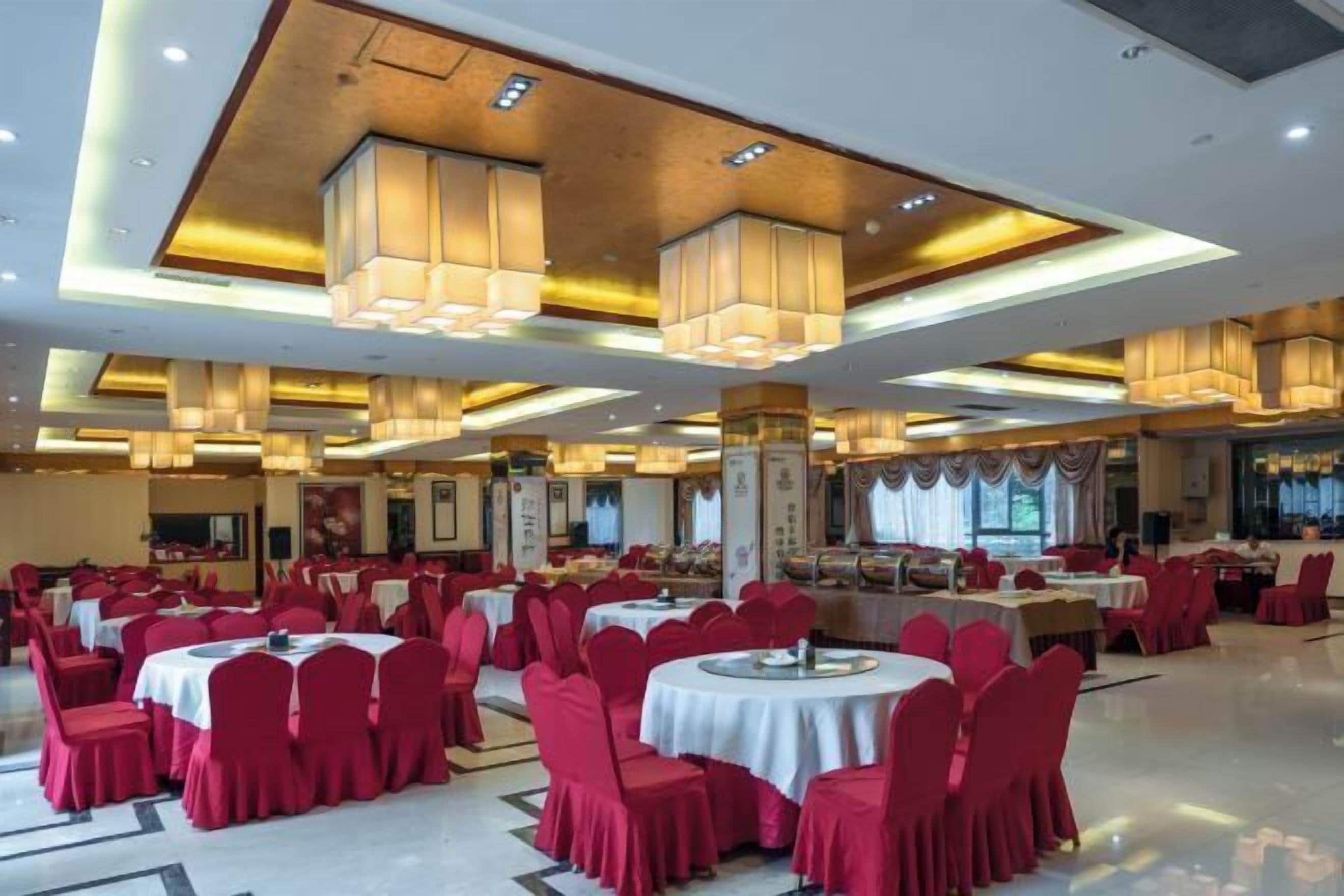 Une salle de banquet avec des tables rondes, des chaises rouges et des lustres modernes.