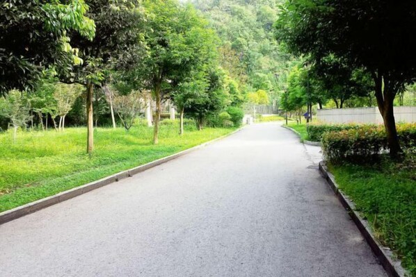 A paved pathway flanked by trees and grass, leading into a forested area. - Haohan Hotel (Changshun)