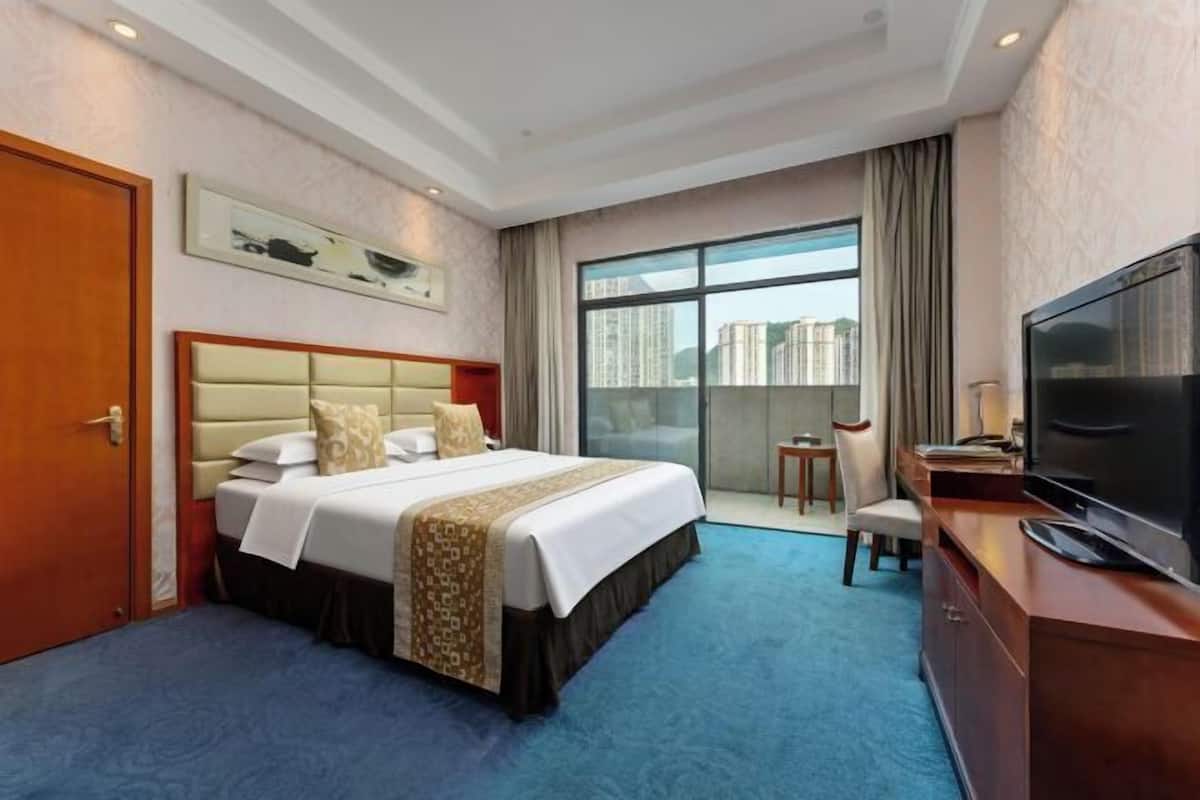 A hotel room with a bed, a television, a desk, and a window with a city view.