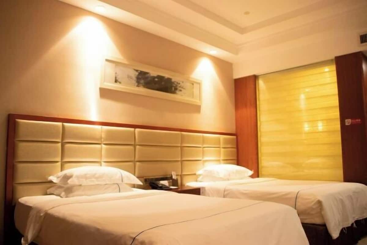 A hotel room with two beds, a headboard, a shelf with artwork, and a closed door.