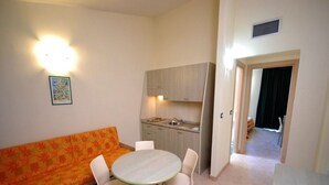A compact living space with a sofa, dining table, chairs, a kitchenette, and a hallway leading to another room. - Residence Borgoverde Two-room Apartment 5 Pax (Imperia)
