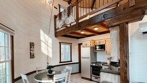 Una cocina amplia con vigas de madera, un comedor con sillas blancas y vistas al exterior.