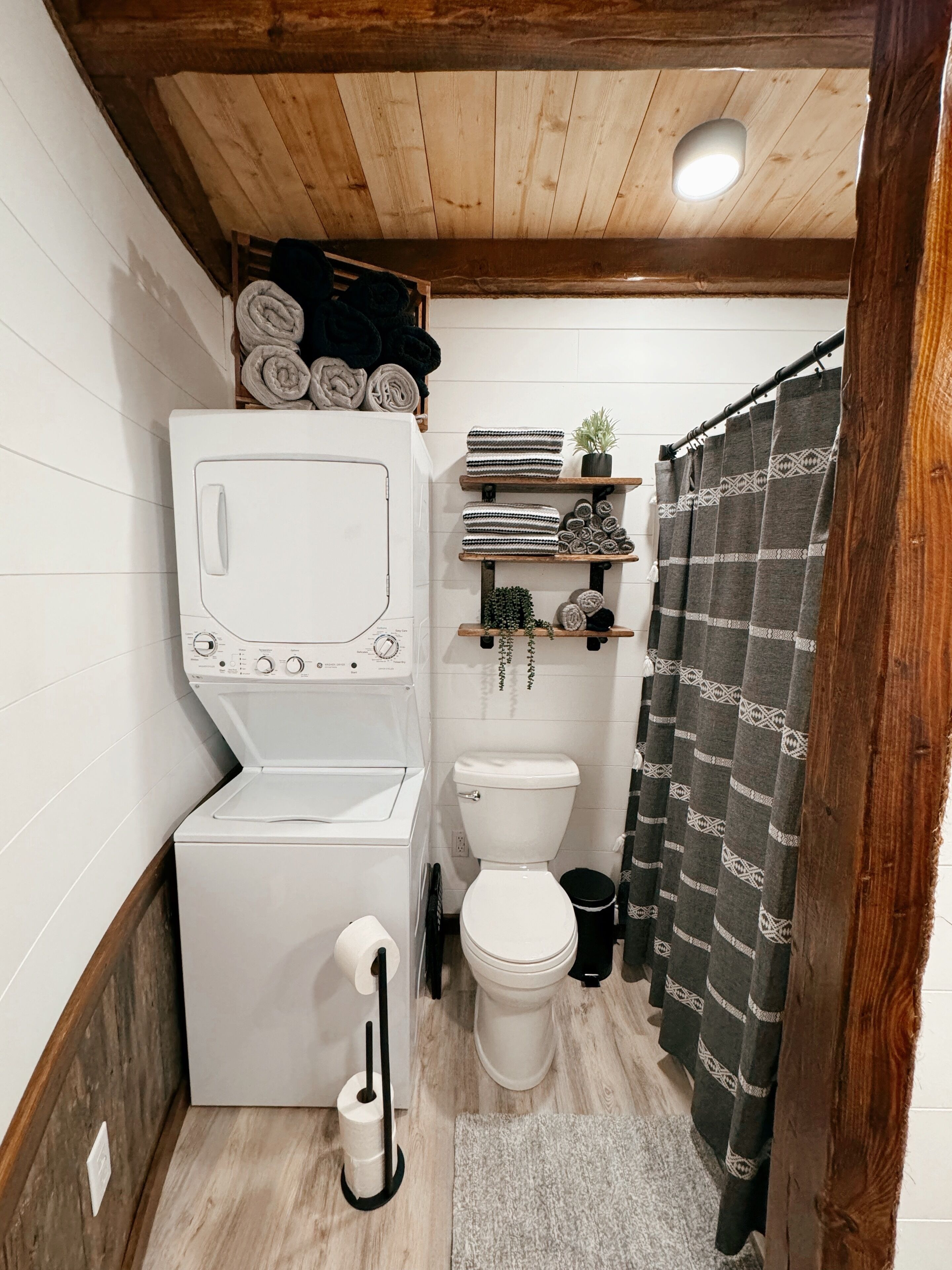 Un baño compacto con lavadora, inodoro y estantes con toallas y plantas.